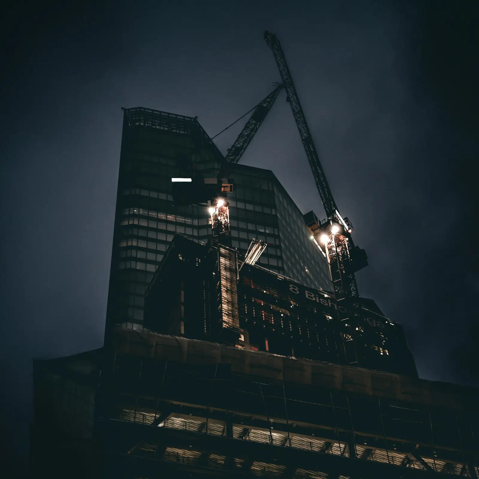A tower under construction at night, crane lights glowing
